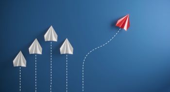 Cinq avions en papier, dont quatre blancs et volant dans la même direction, et un rouge prenant une autre direction